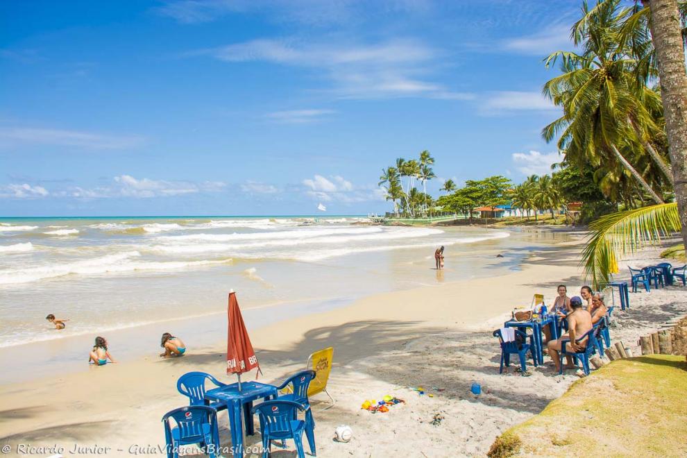 Imagem de uma família nas cadeiras do quiosque e crianças na beira do mar.